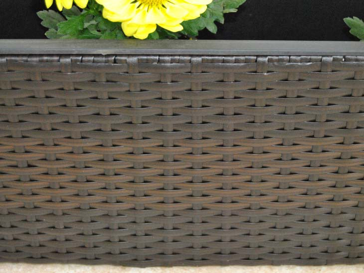 Nahaufnahme des Geflechts eines rechteckigen Pflanzkübels aus Polyrattan in Coffee Braun mit gelben Blüten